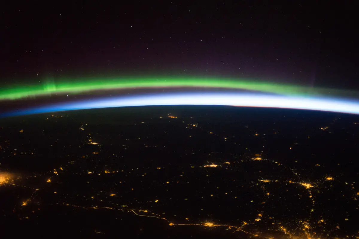 The northern lights over northern Europe at night, seen from the International Space Station, with city lights below.